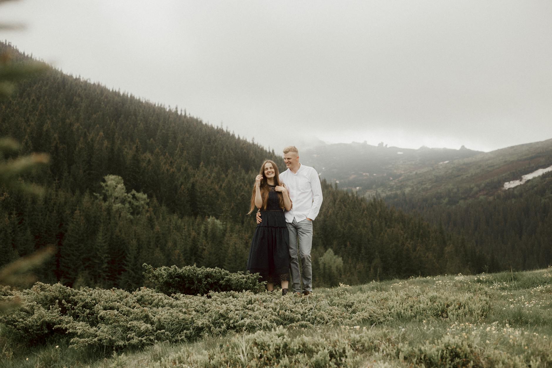 Para spaceruje po zielonej górskiej łące pod pochmurnym niebem